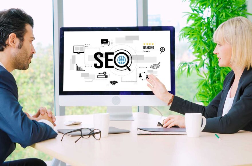 Zwei Geschäftsleute besprechen am Schreibtisch eine SEO-Strategie, sichtbar auf einem Monitor mit